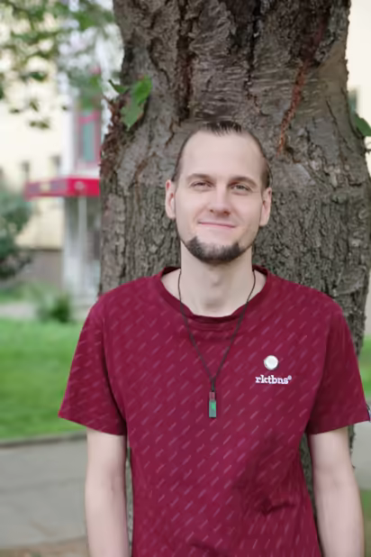 ich, lächelnd, mit zusammengebundenen Haaren, an einem Baum lehnend